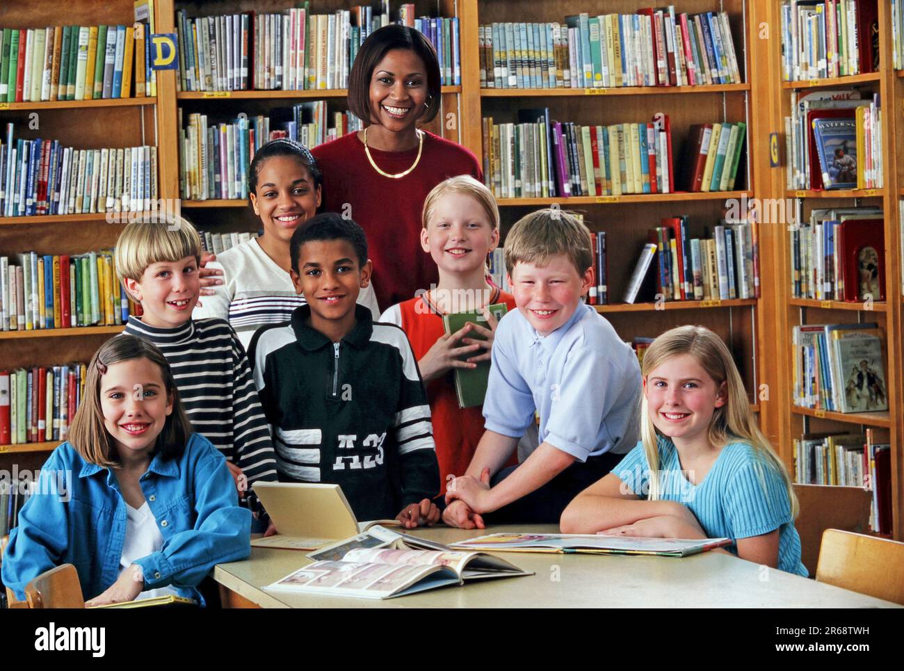 Ritratto di un bibliotecario di scuola elementare afro-americano nella biblioteca scolastica con un gruppo di alunni di razza mista Foto Stock