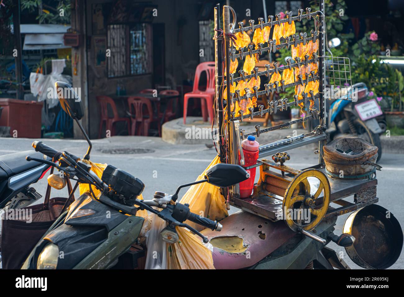 Il calamaro secco pressato appende da un supporto montato su una moto di un venditore di strada alla luce del tramonto, Thailandia Foto Stock