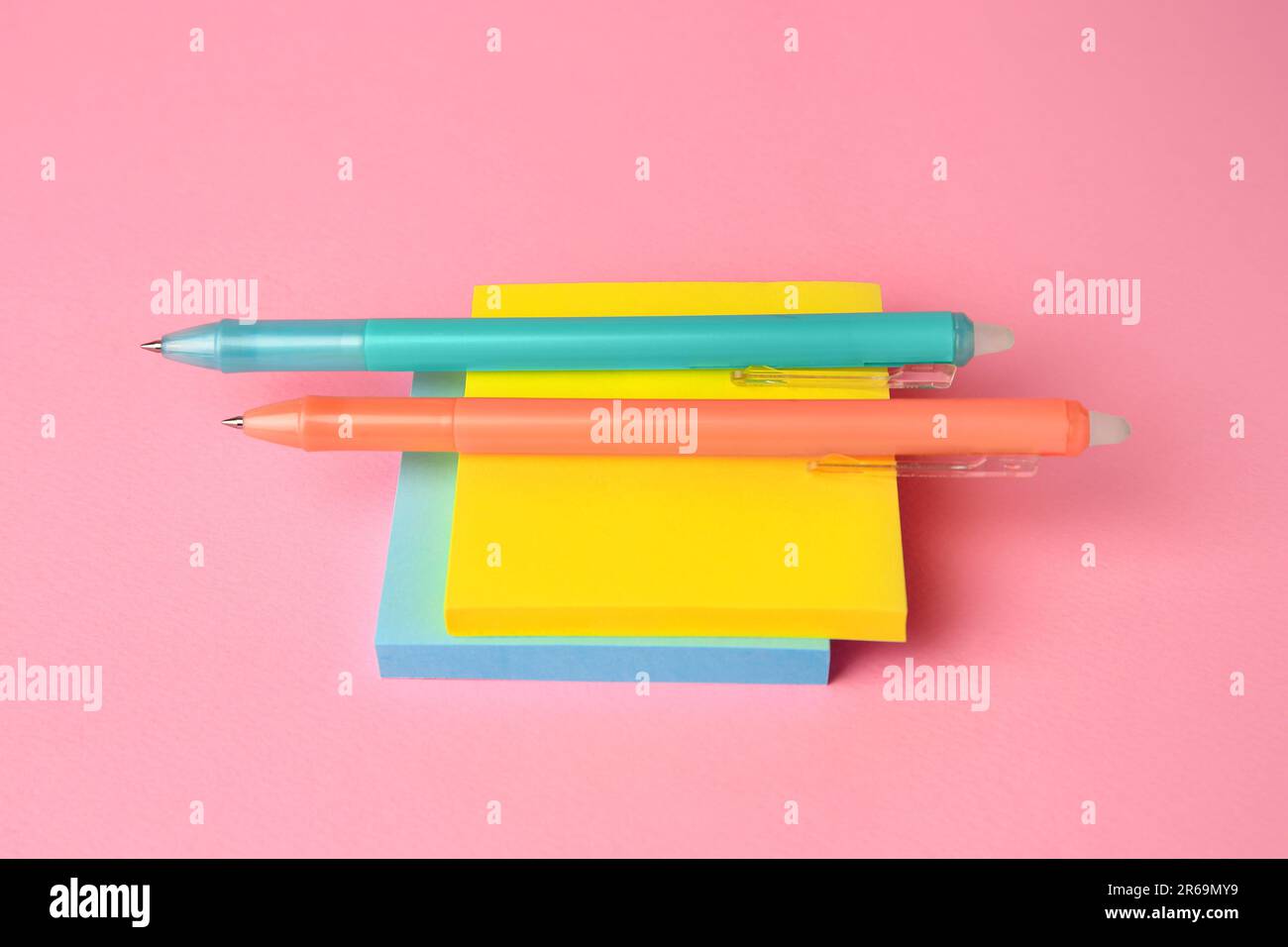 Note di carta colorate con penne cancellabili su sfondo rosa