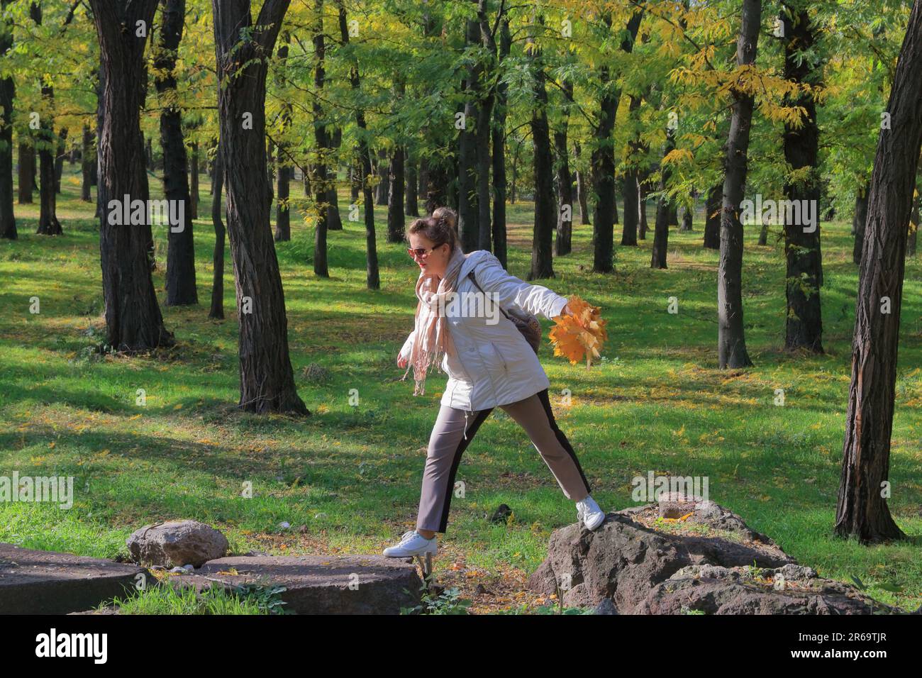 Nella foto, una giovane donna salta da pietra a pietra nella foresta autunnale. Foto Stock