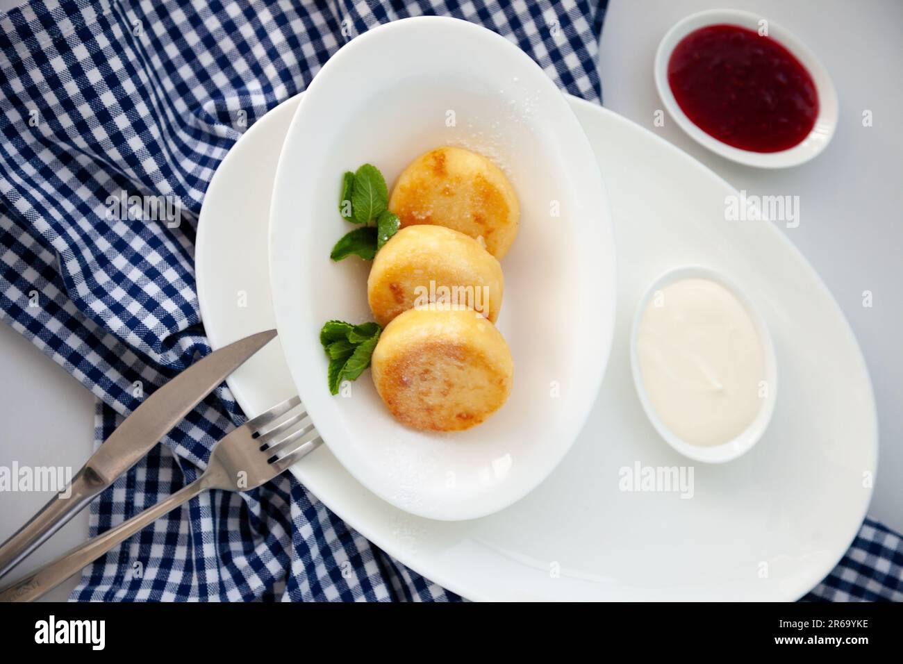 Frittelle di formaggio ricotta rotonda in un piatto bianco su sfondo blu. Cibo prima colazione. Cibo sano. Salsa di panna acida e menta. Primo piano vista dall'alto. Pasto dessert. Frittelle di ricotta al formaggio ricotta. Foto Stock