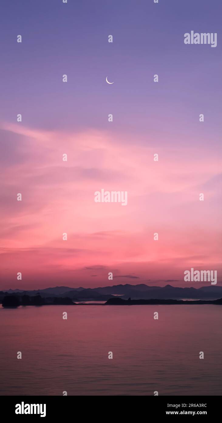 Immagine verticale, luna crescente in un cielo dai colori vibranti con silhouette paesaggio di montagne e lago, crepuscolo, sfondo natura carta da parati Foto Stock