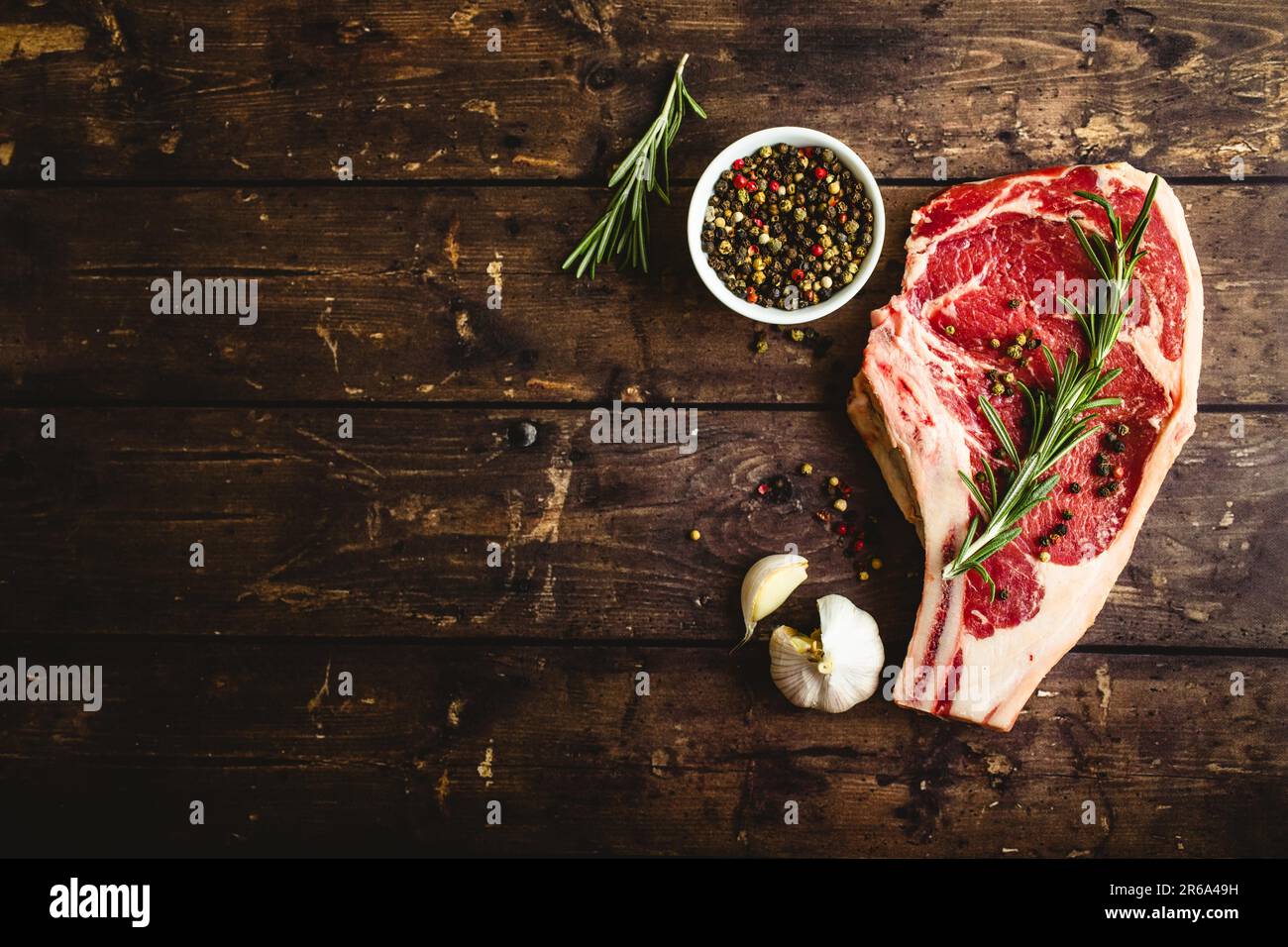 Bistecca di carne cruda marmorizzata, pepe, erbe aromatiche, aglio, vecchio sfondo di legno. Spazio per il testo. Bistecca di manzo pronta per la cottura. Vista dall'alto. Spazio di copia. Foto Stock