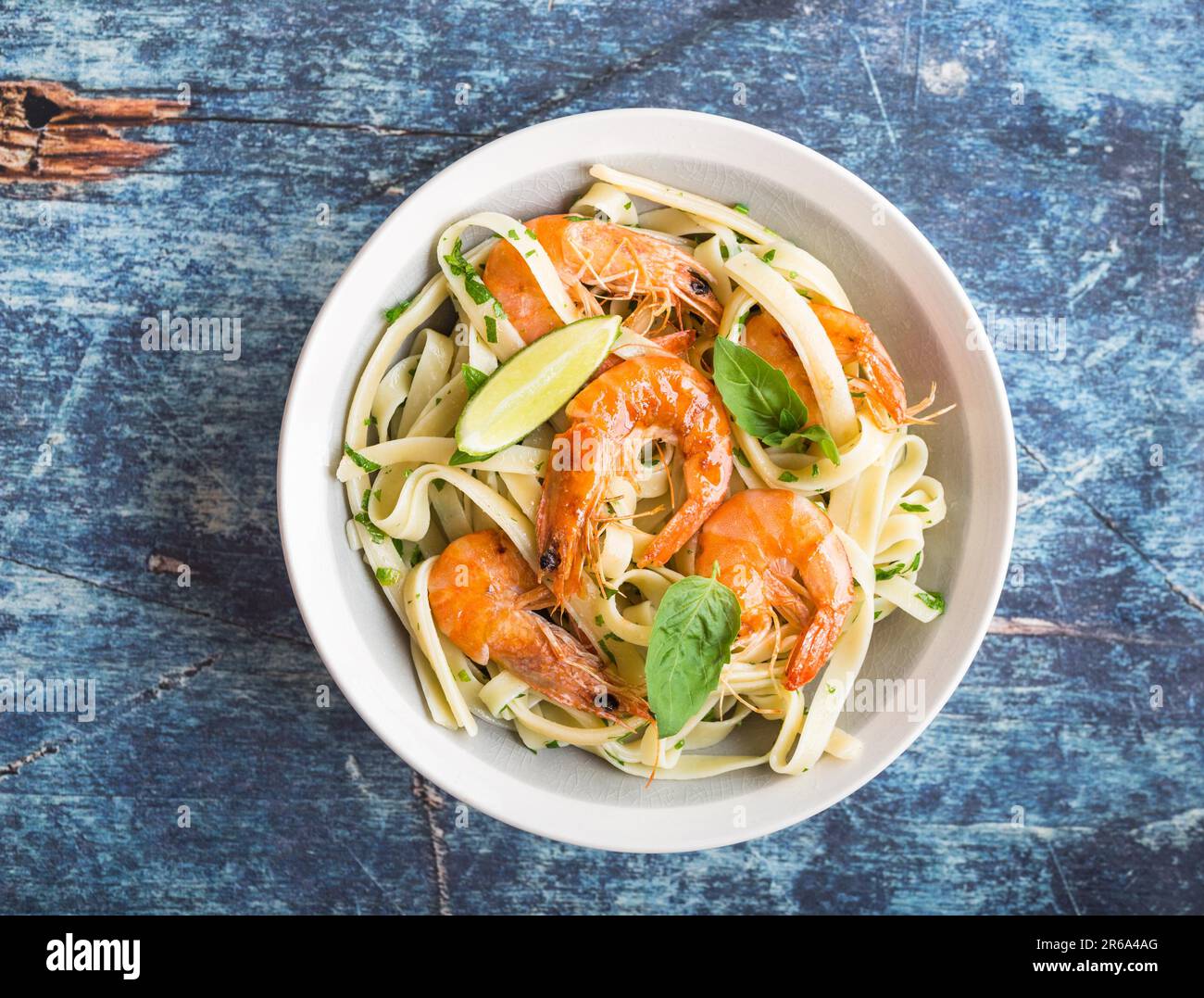 Pasta fatta in casa con gamberetti fritti e basilico su sfondo rustico di legno blu. Pasta con frutti di mare in piatto. Vista dall'alto. Primo piano. Cucina mediterranea. Foto Stock