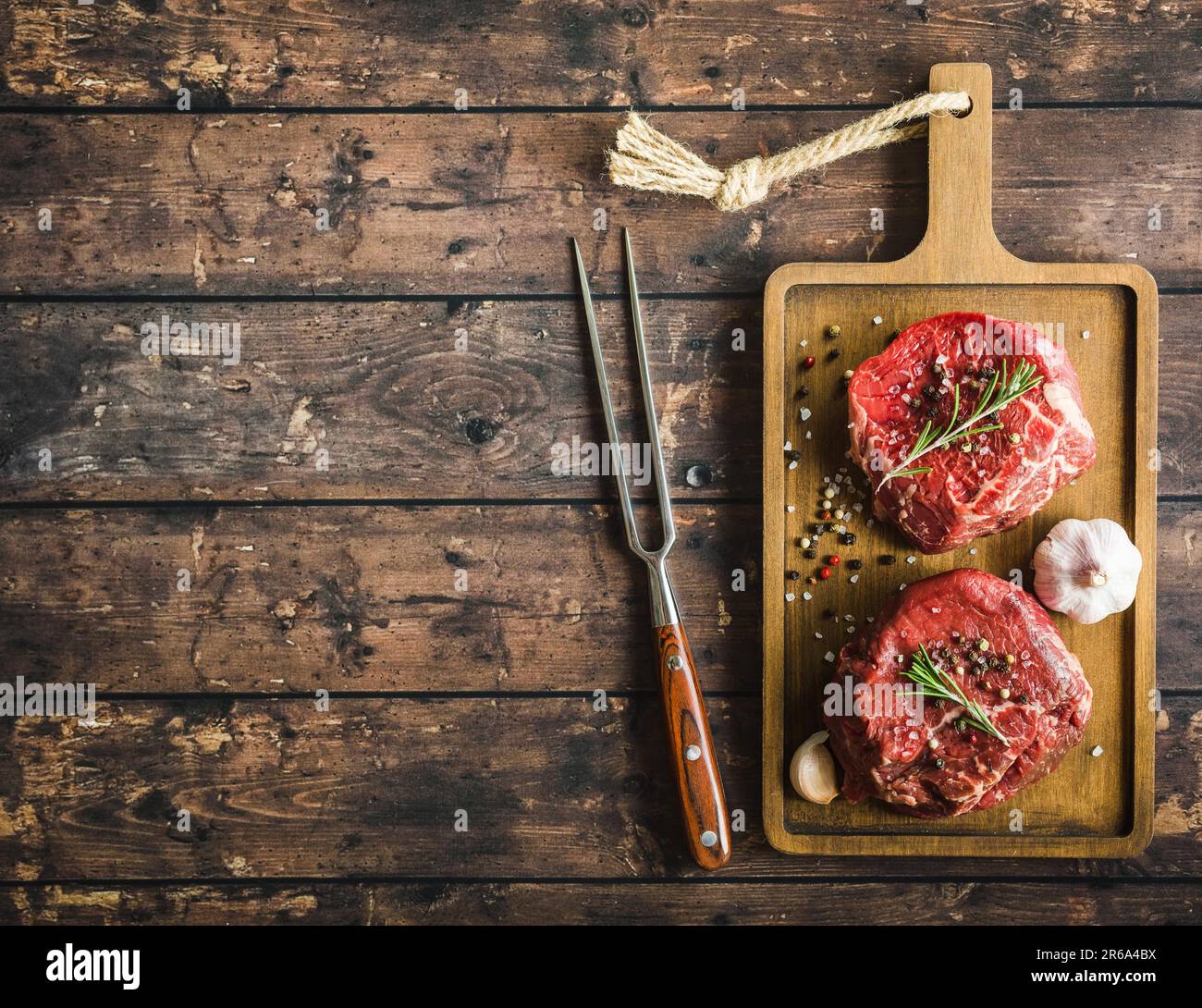 Bistecca di carne cruda in marmo Filet Mignon con condimenti, forchetta, tagliere in legno. Spazio per il testo. Bistecca di manzo pronta per la cottura. Vista dall'alto. Ingredienti. Foto Stock