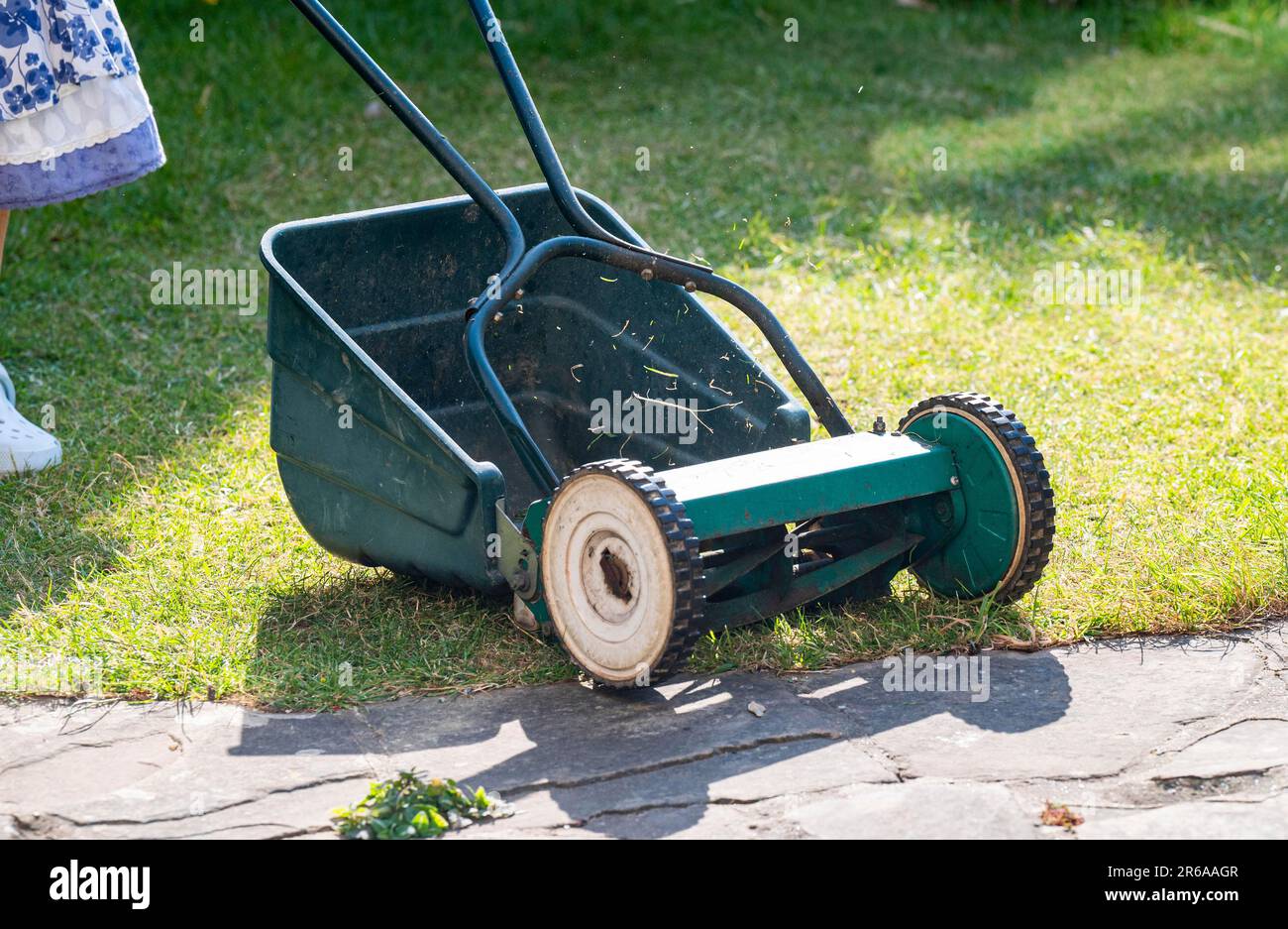 Donna che utilizza un rasaerba a mano taglio piccolo città urbano giardino prato erba lasciando parte dell'erba non tagliato intorno ai bordi per aiutare la fauna selvatica Foto Stock