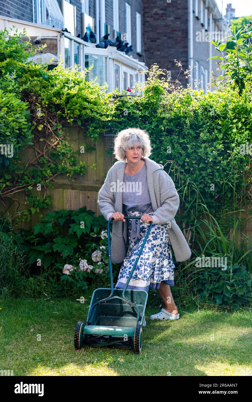 Donna che utilizza un rasaerba a mano taglio piccolo città urbano giardino prato erba lasciando parte dell'erba non tagliato intorno ai bordi per aiutare la fauna selvatica Foto Stock