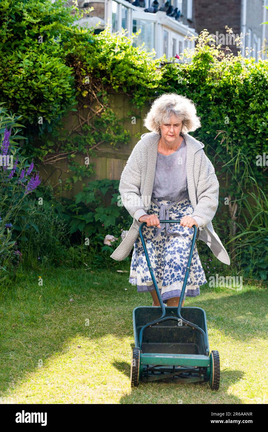 Donna che utilizza un rasaerba a mano taglio piccolo città urbano giardino prato erba lasciando parte dell'erba non tagliato intorno ai bordi per aiutare la fauna selvatica Foto Stock