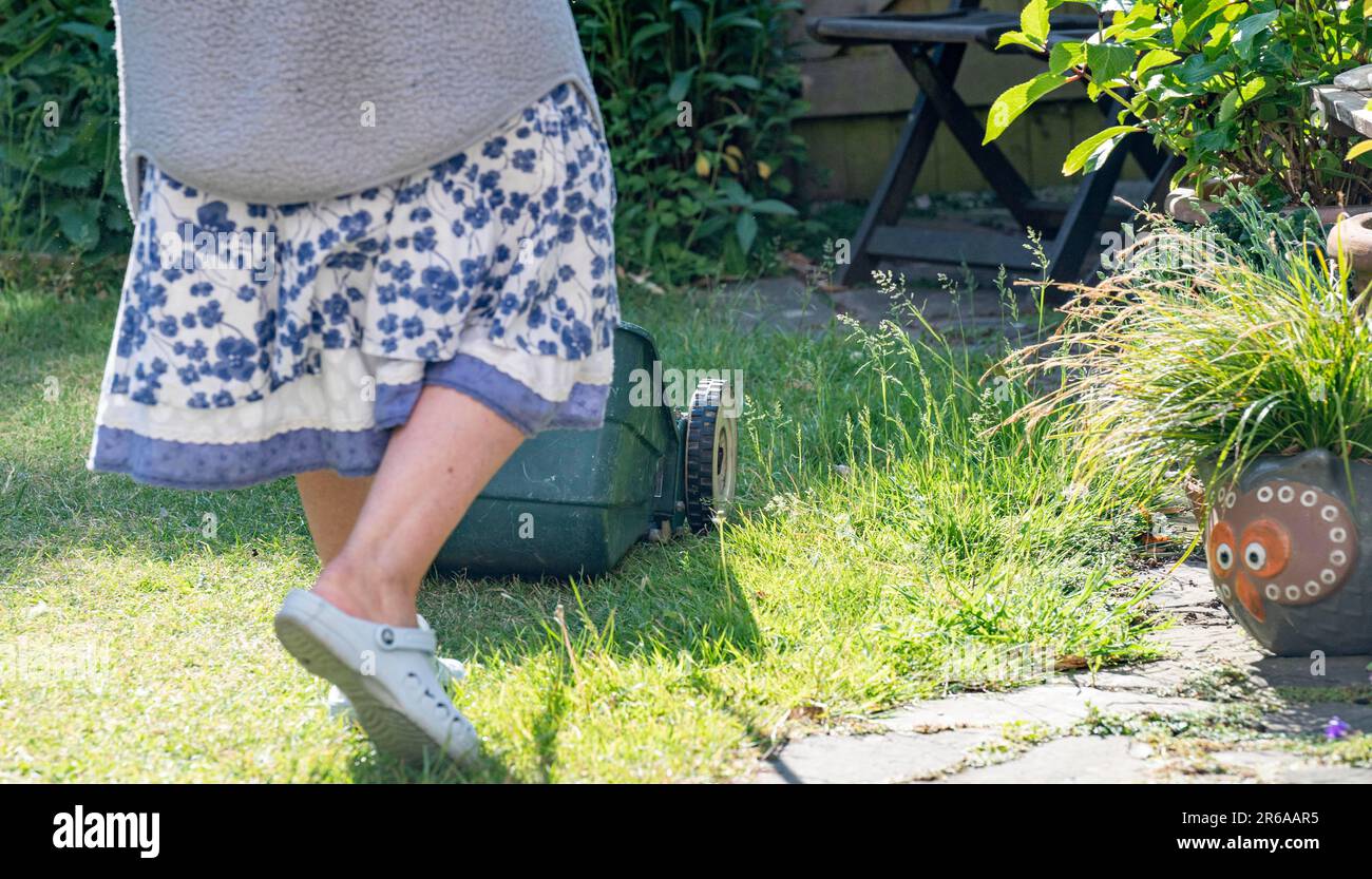 Donna che utilizza un rasaerba a mano taglio piccolo città urbano giardino prato erba lasciando parte dell'erba non tagliato intorno ai bordi per aiutare la fauna selvatica Foto Stock