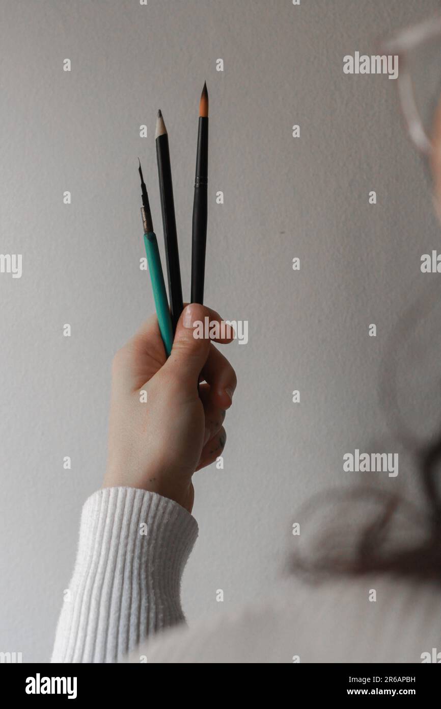 Mani di donna che tengono i pennelli. Concetto di una persona che pensa al suo prossimo pezzo d'arte Concetto di pittura e processo creativo. Foto Stock