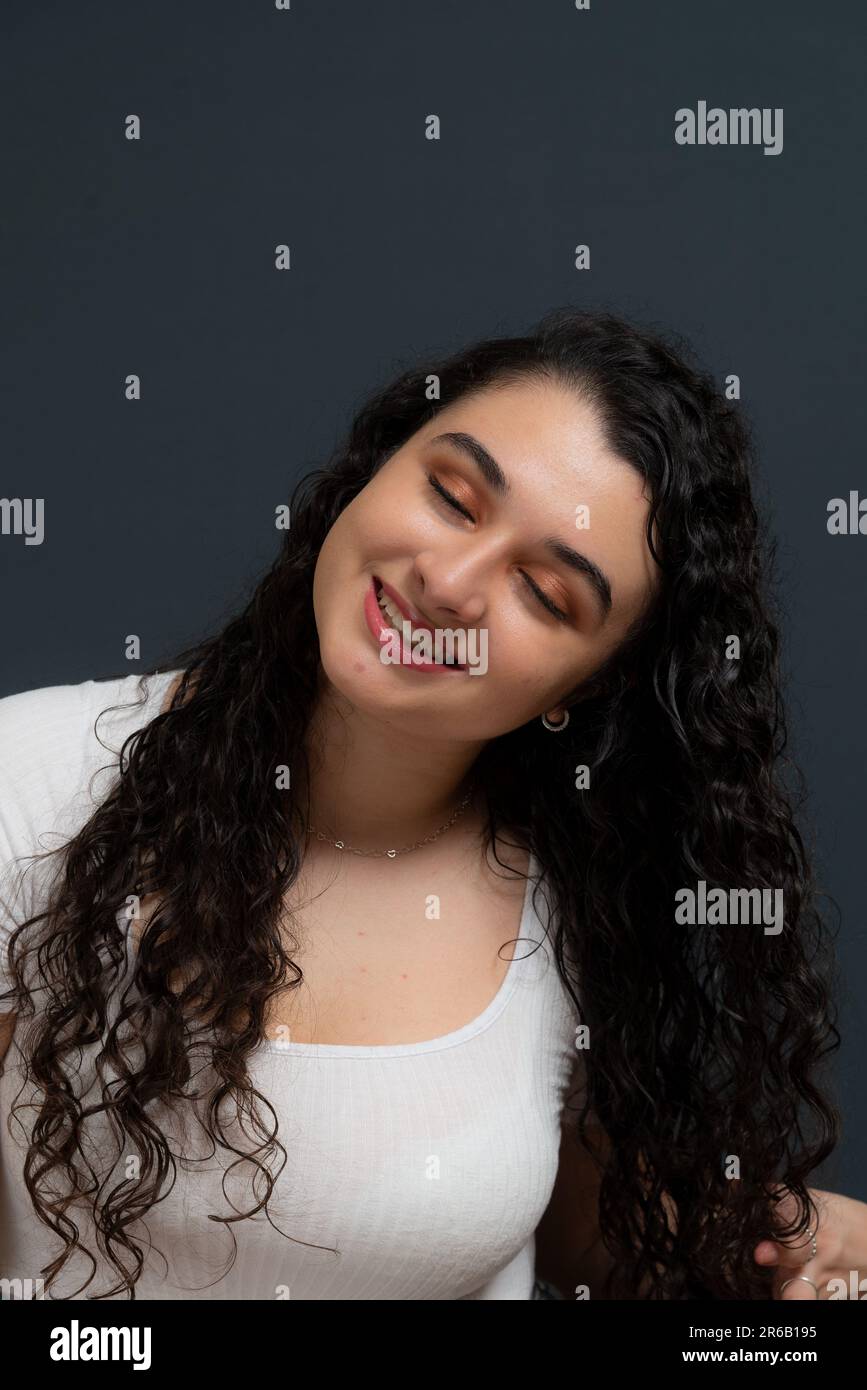 Una donna felice con i capelli castani ricci sorridenti luminosi, di fronte alla macchina fotografica Foto Stock