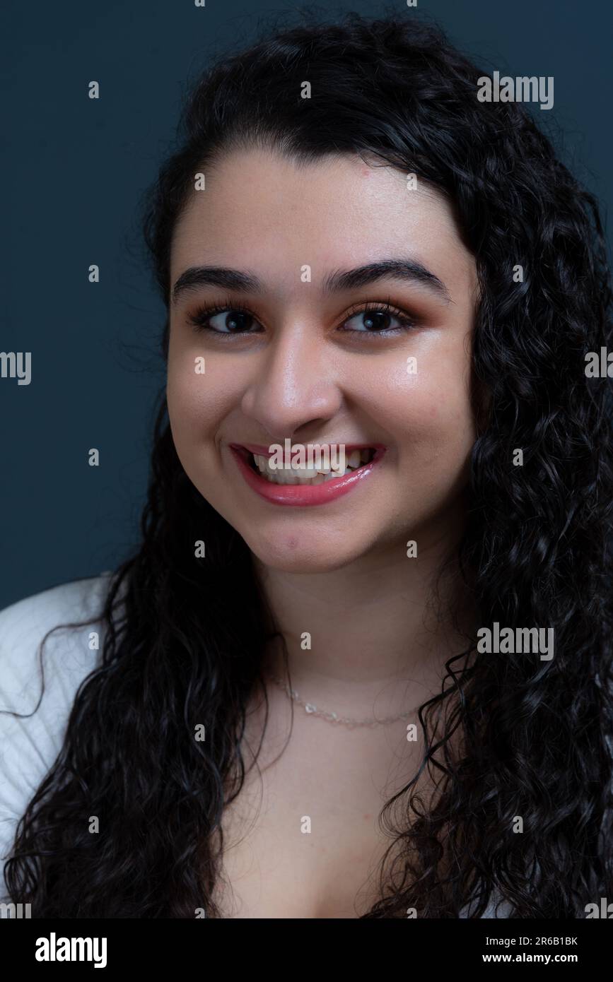 Una donna felice con i capelli castani ricci sorridenti luminosi, di fronte alla macchina fotografica Foto Stock