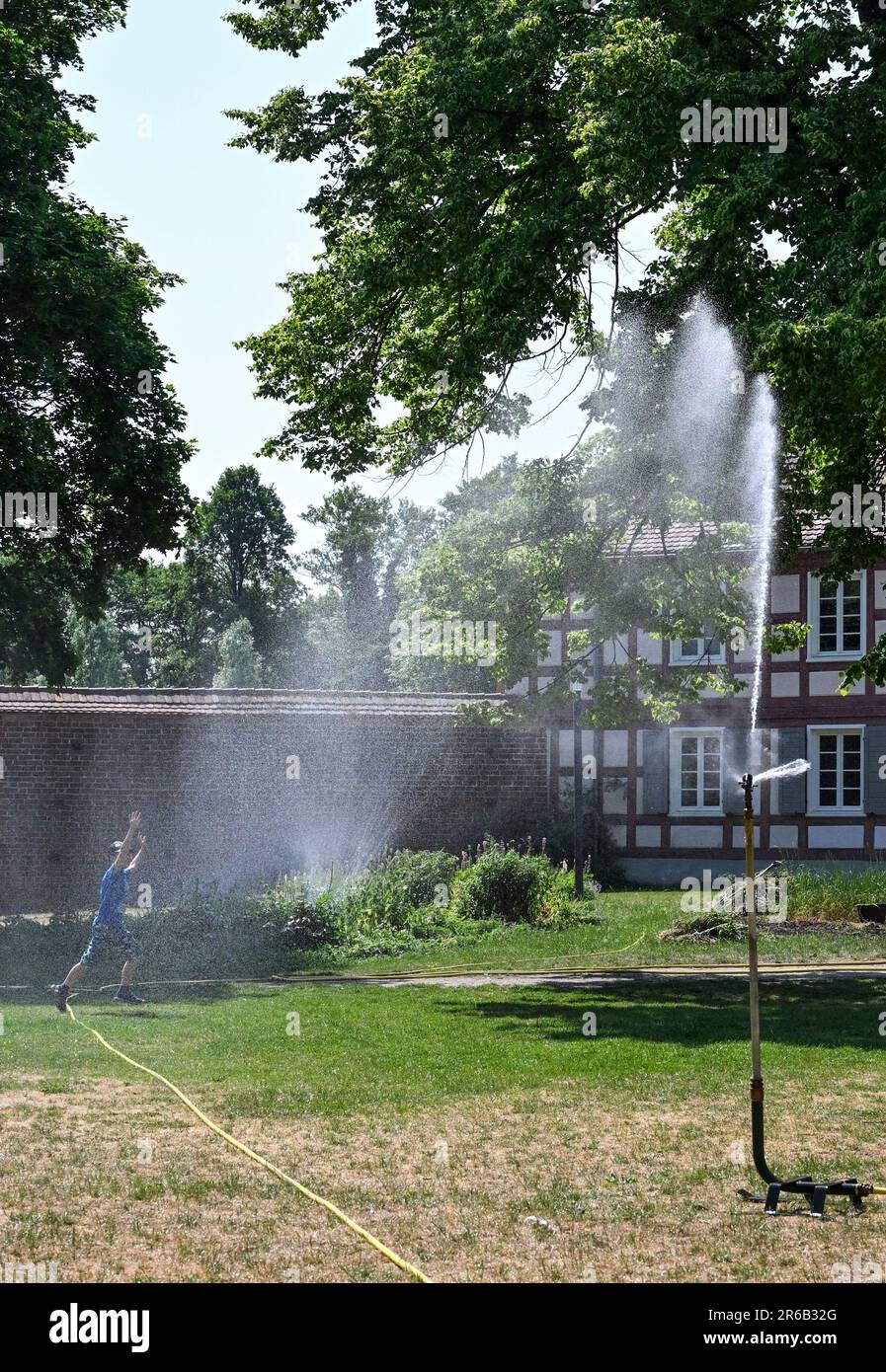 08 giugno 2023, Brandeburgo, Wittstock/Dosse: Nel cortile del vecchio castello vescovile, un irrigatore per prato fornisce acqua al prato e ai aiuole. L'acqua è anche volentieri presa come rinfresco. Foto: Jens Kalaene/dpa Foto Stock