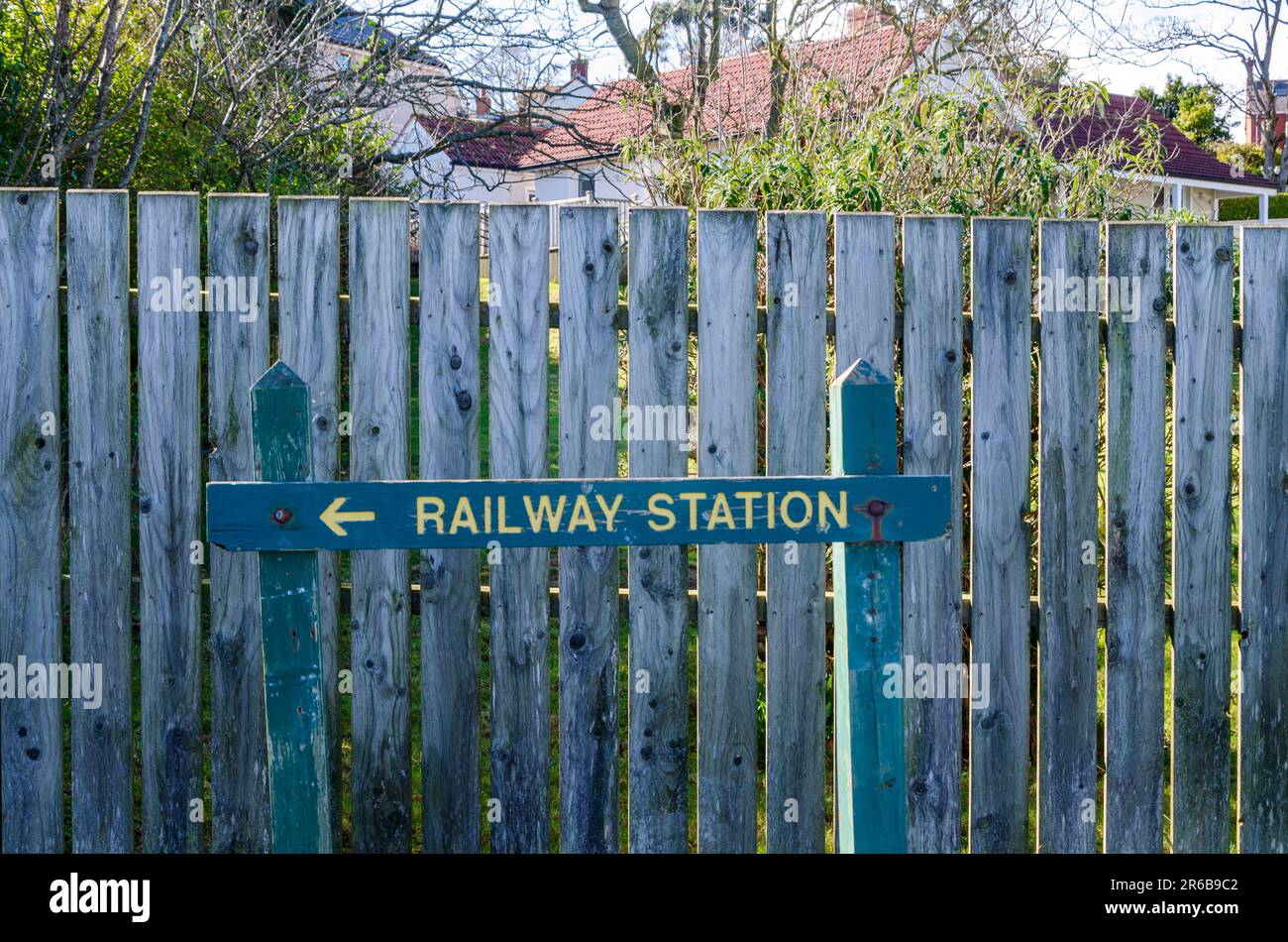 Cartello di legno che indica la stazione ferroviaria locale a Helens Bay un piccolo villaggio County Down in Irlanda del Nord con una recinzione blu sullo sfondo Foto Stock