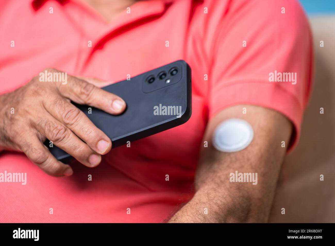 Primo piano di un uomo anziano che controlla il livello di zucchero o glucosio toccando il telefono cellulare per il sensore a casa - concetto di tecnologia, diabete e salute Foto Stock