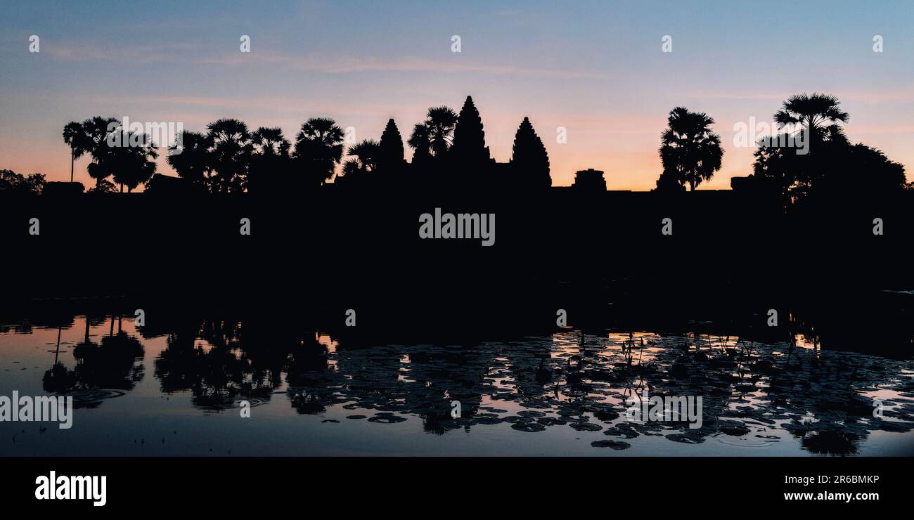 Scopri il fascino etereo di Angkor Wat all'alba, dove il cielo scuro e le silhouette degli alberi aggiungono un tocco di misticismo al paesaggio cambogiano. Foto Stock