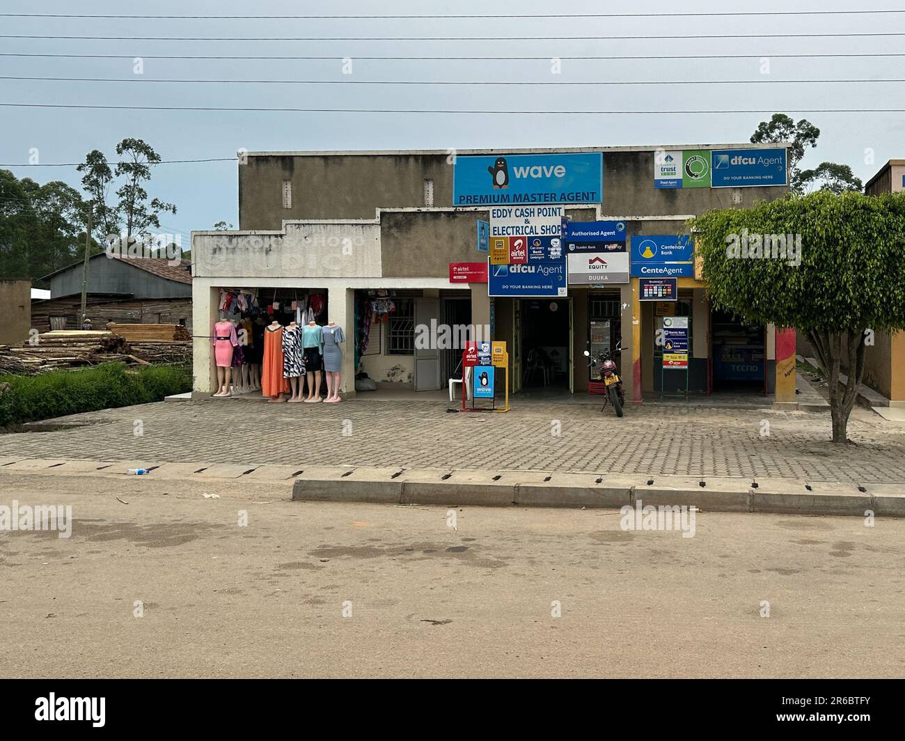 Ntungamo, Uganda - 25 marzo 2023: Tipici edifici di villaggio di mercato su strada, vendita di abbigliamento e servizi bancari Foto Stock