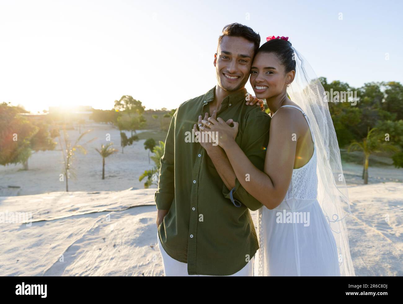 Coppia caucasica in nubilato che mostra anelli di nozze mentre si è in piedi in spiaggia contro il cielo limpido Foto Stock