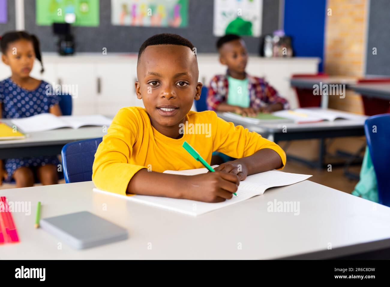 Ritratto di felice scolaro africano americano elementare seduto alla scrivania in classe Foto Stock