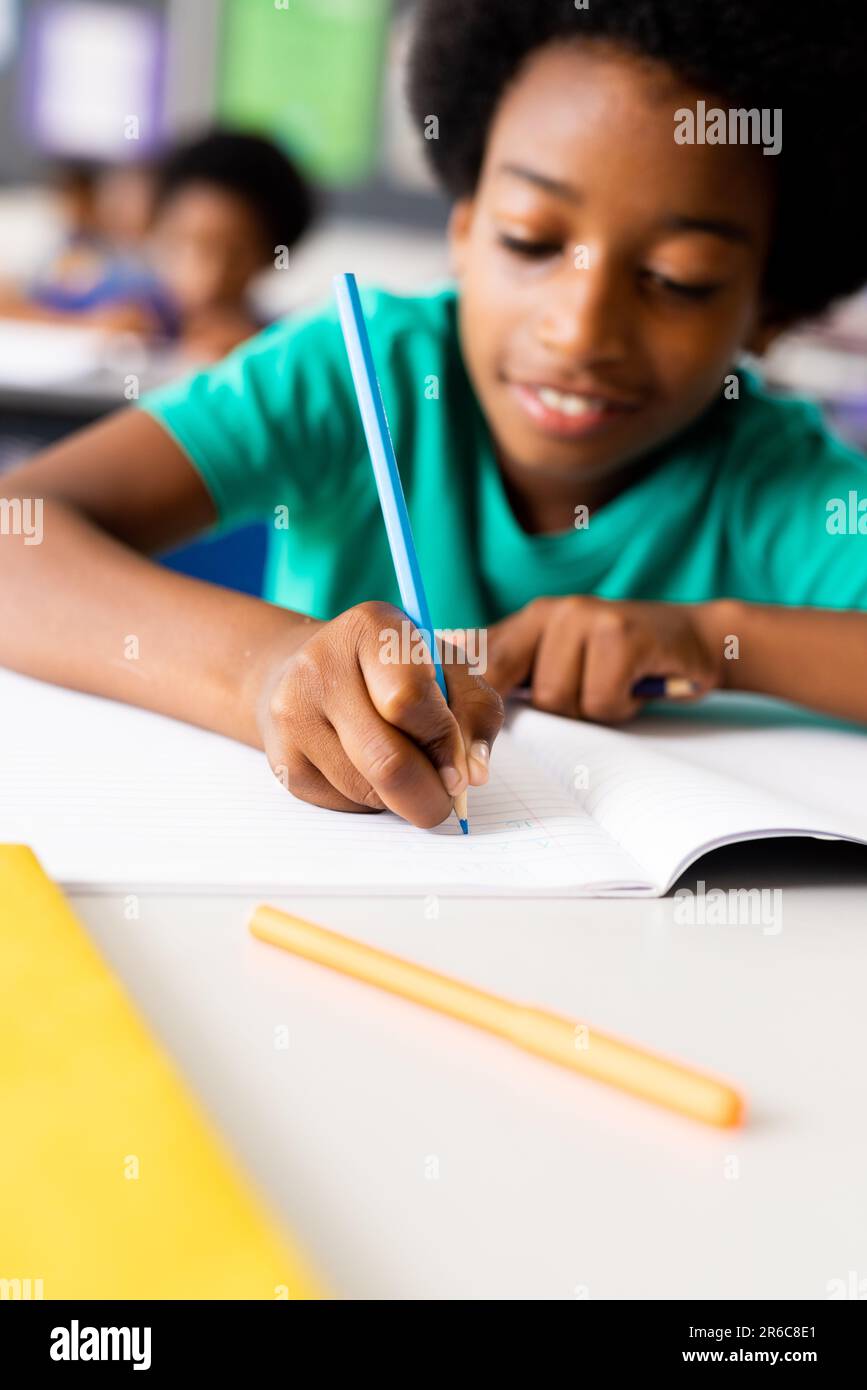 Ritratto di happy afroamericano scuola elementare scrittura in notebook alla scrivania in classe Foto Stock