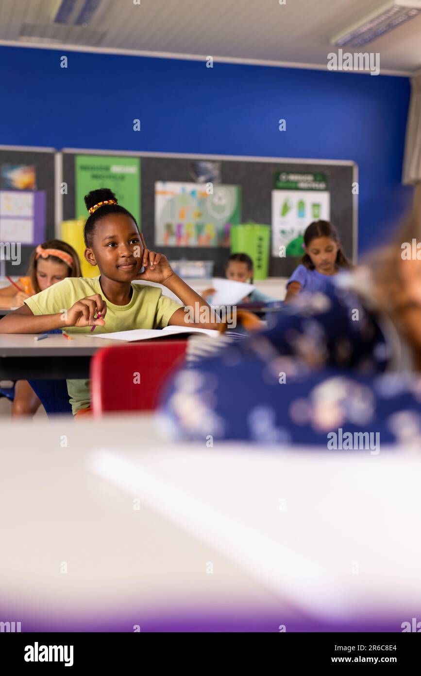 Buone studentesse diverse che ascoltano alle scrivanie della classe elementare Foto Stock