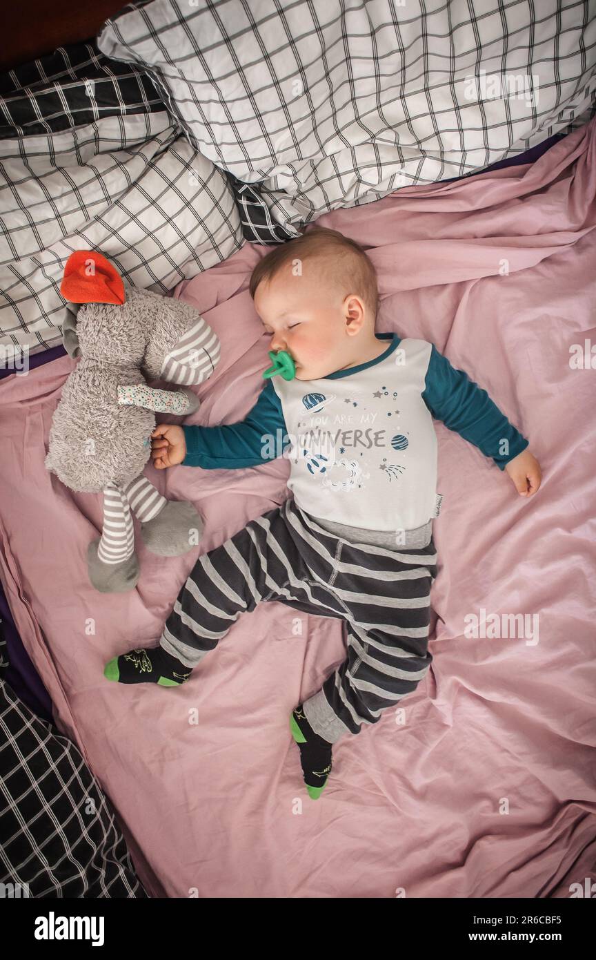 Un bambino grazioso sta dormendo pacificamente e si rilassa sul suo letto con i giocattoli. Vista dall'alto della culla. Amore ed emozioni familiari Foto Stock