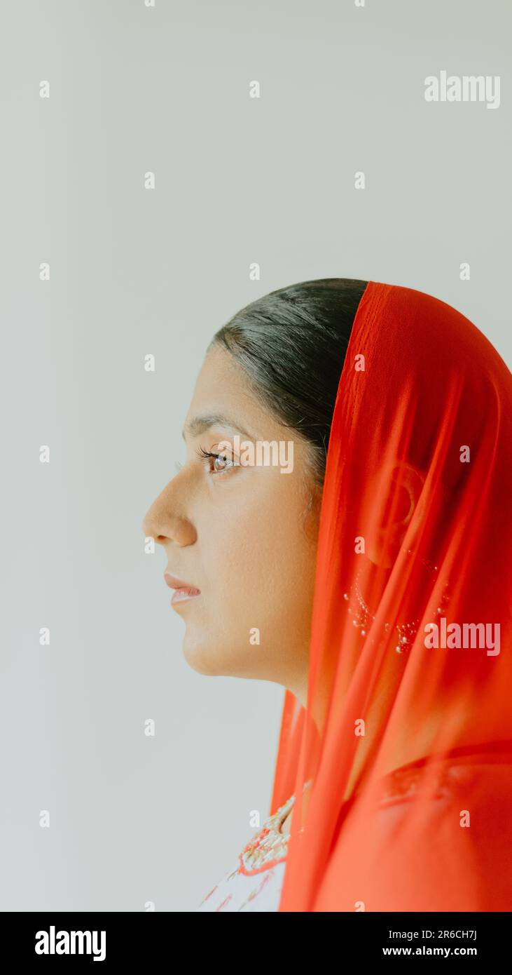 Una donna indiana in un ritratto con profilo laterale con un vivace velo rosso, il suo volto si distingue guardando lontano dalla fotocamera Foto Stock