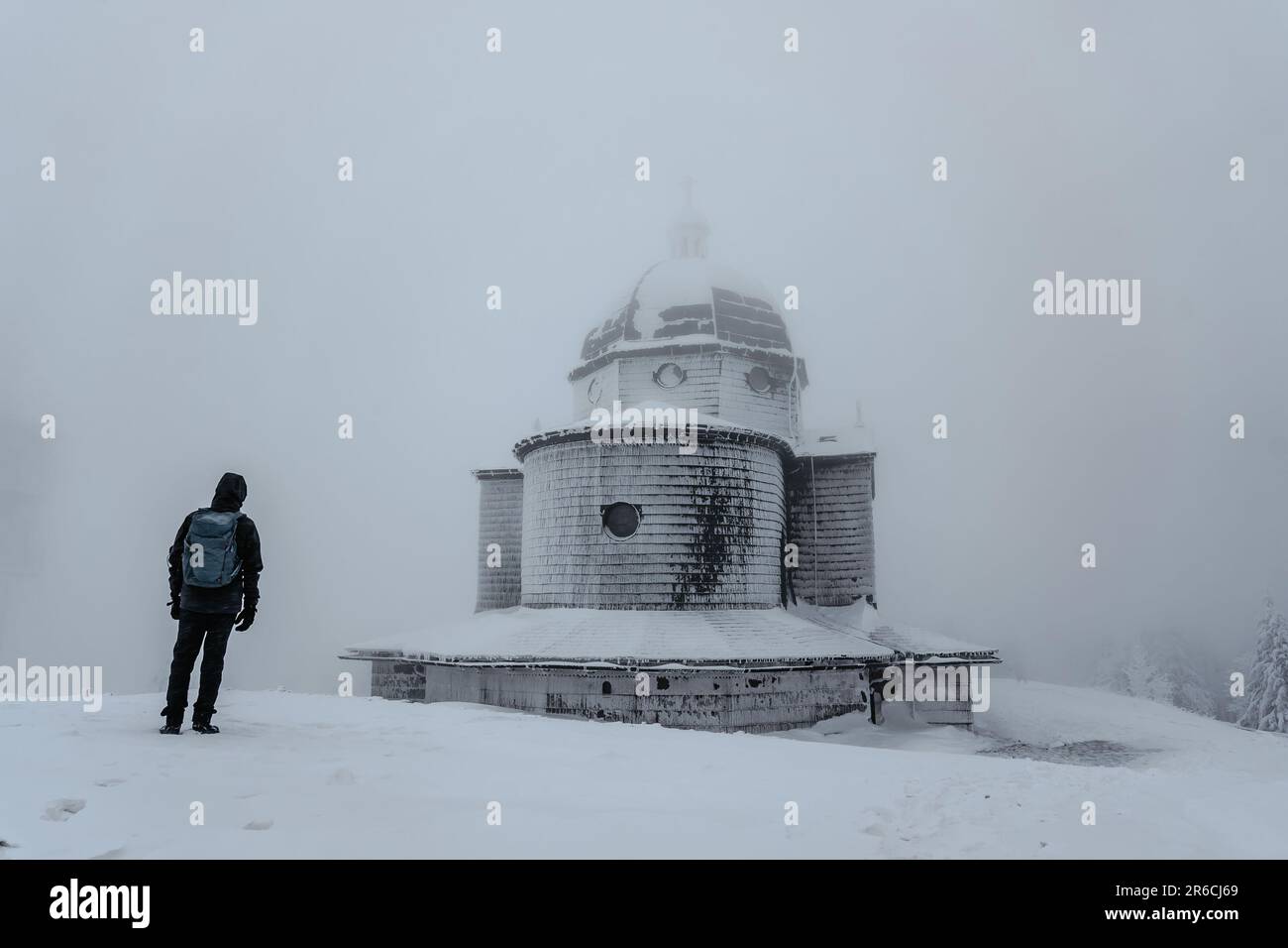 Uomo solitario in piedi sulla montagna Radhost guardando alla Cappella di San Cirillo e Metodio, Beskids, repubblica Ceca. Silhouette dell'uomo nel paesaggio invernale, fogg Foto Stock