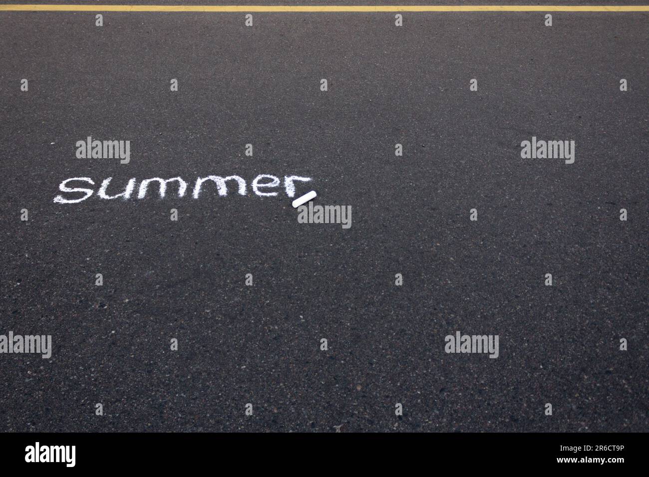 La parola estate scritta su asfalto nero con gesso bianco, con una linea gialla di marcatura stradale in cima alla foto. Foto Stock