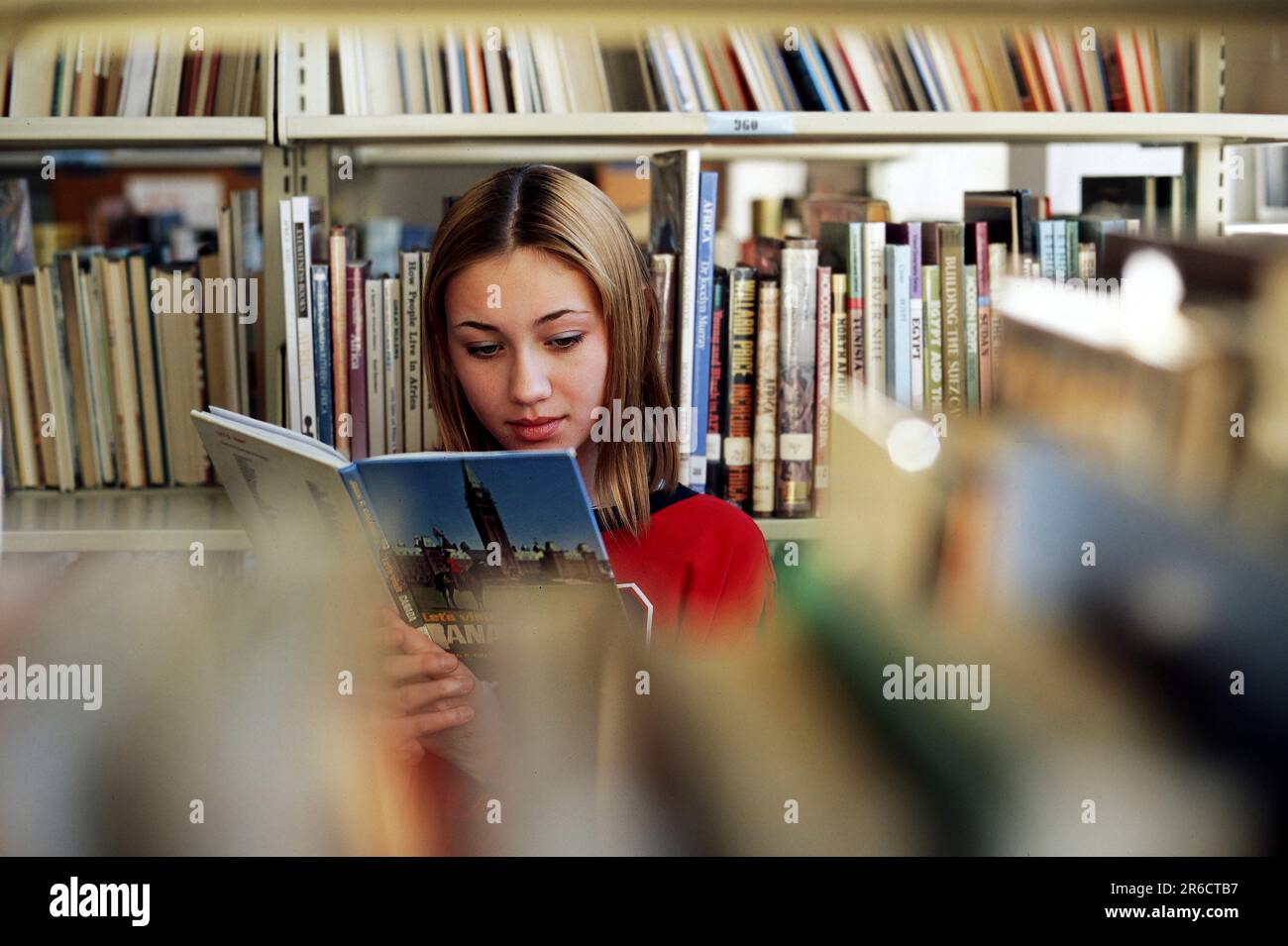 Studentessa caucasica di scuola media che guarda un libro della biblioteca scolastica Foto Stock