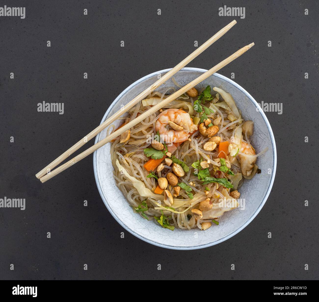 Gamberetti freschi, spaghetti saporiti, verdure nutrienti e arachidi croccanti serviti in un'elegante ciotola bianca con bastoncini. Foto Stock