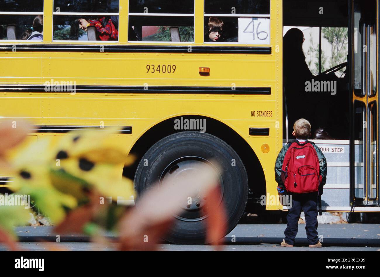 Studente di scuola elementare che indossa un grande zaino che si prepara a salire a bordo di uno scuolabus il primo giorno di scuola Foto Stock