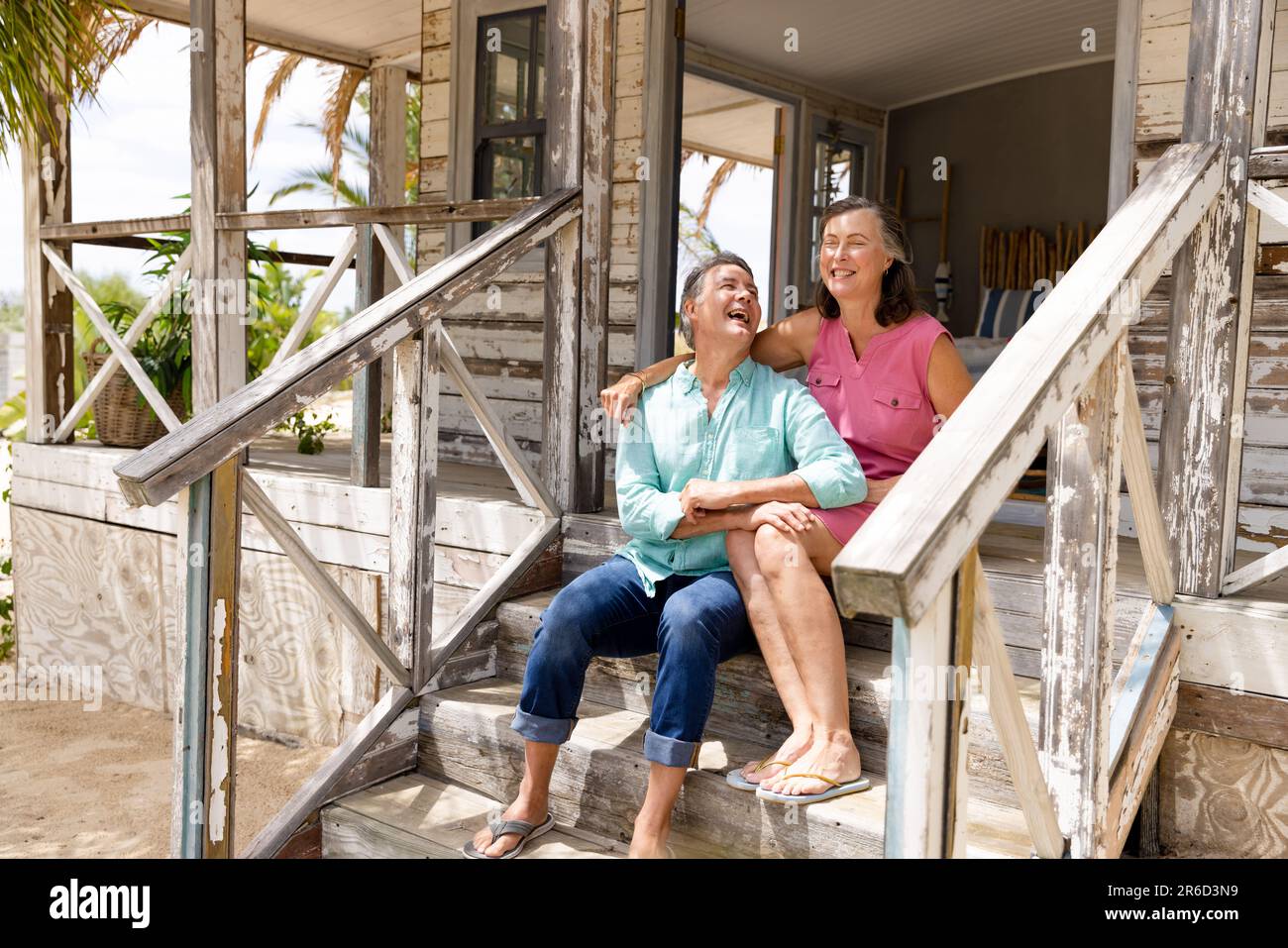 Ecstatic coppia caucasica senior parlando e ridendo mentre si siede sulla scala fuori cottage Foto Stock