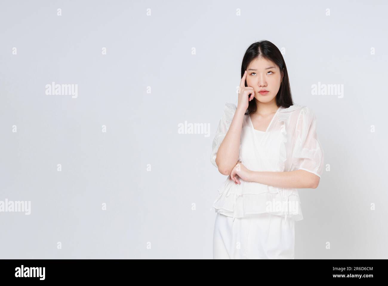 Giovane donna in piedi e pensando con faccia seria isolata su sfondo bianco. Foto Stock