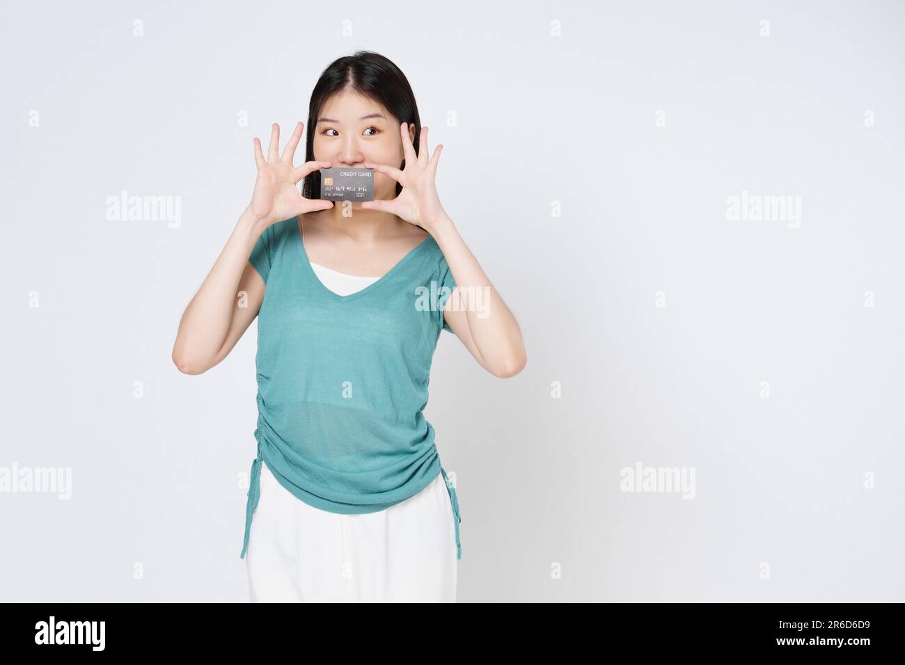 Giovane donna che tiene la mano carta di credito coperchio della bocca isolata su sfondo bianco. Foto Stock