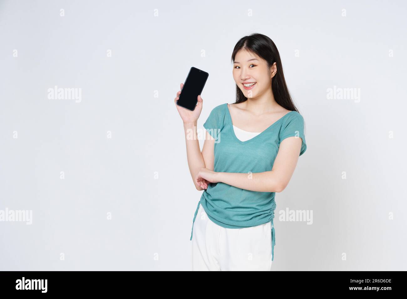 Donna asiatica sorridente che tiene il telefono cellulare mentre è isolata su sfondo bianco. Foto Stock