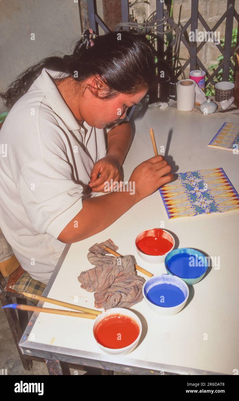 Un'artista femminile che dipinge piastrelle in una fabbrica a Lampang, la terza città più grande del nord della Thailandia. Foto Stock