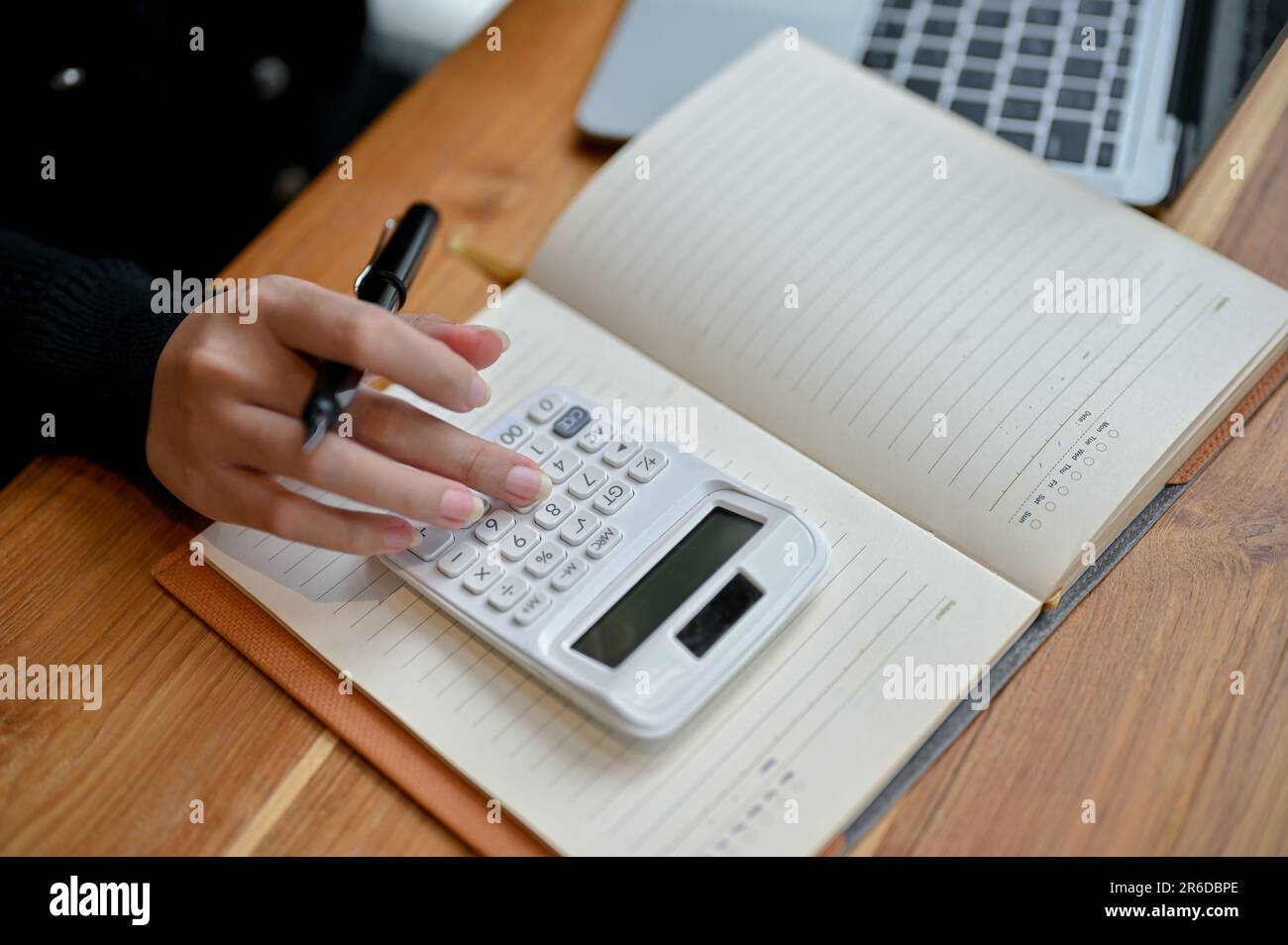 Primo piano immagine dall'alto di una contabile femminile che utilizza una calcolatrice per calcolare e analizzare i dati finanziari, lavorando alla sua scrivania in ufficio. Foto Stock