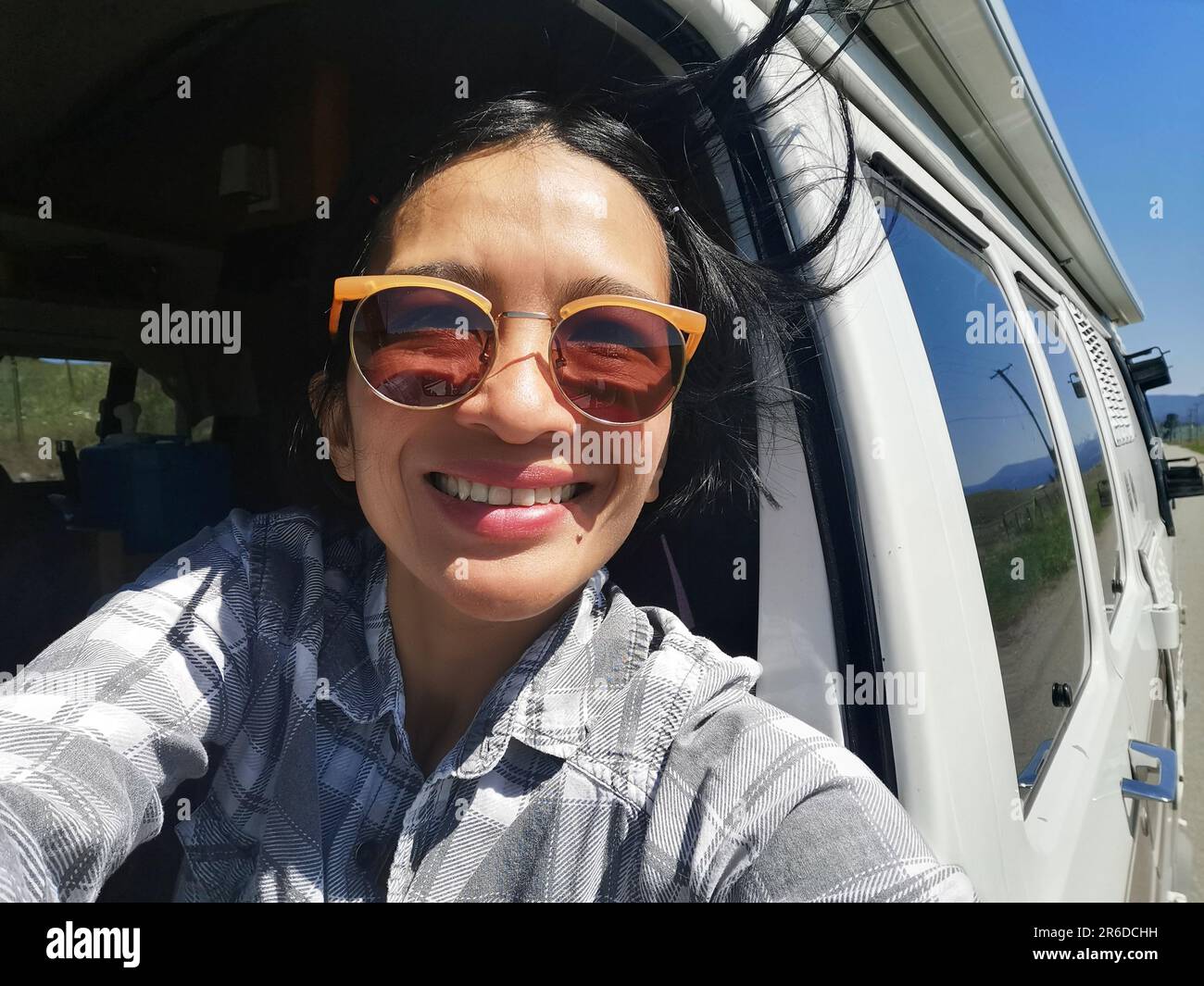 Giovane donna che prende un selfie dal sedile passeggero in un veicolo in movimento in un viaggio su strada a Princeton, British Columbia, Canada. Foto Stock