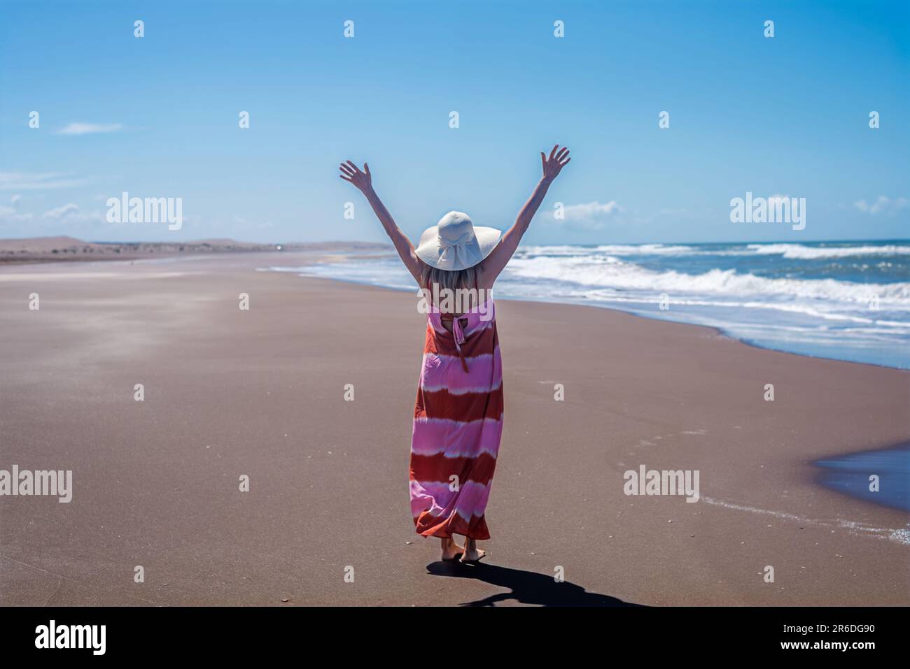 Donna gioiosa che alza le mani mentre si gode la giornata in spiaggia. Foto Stock