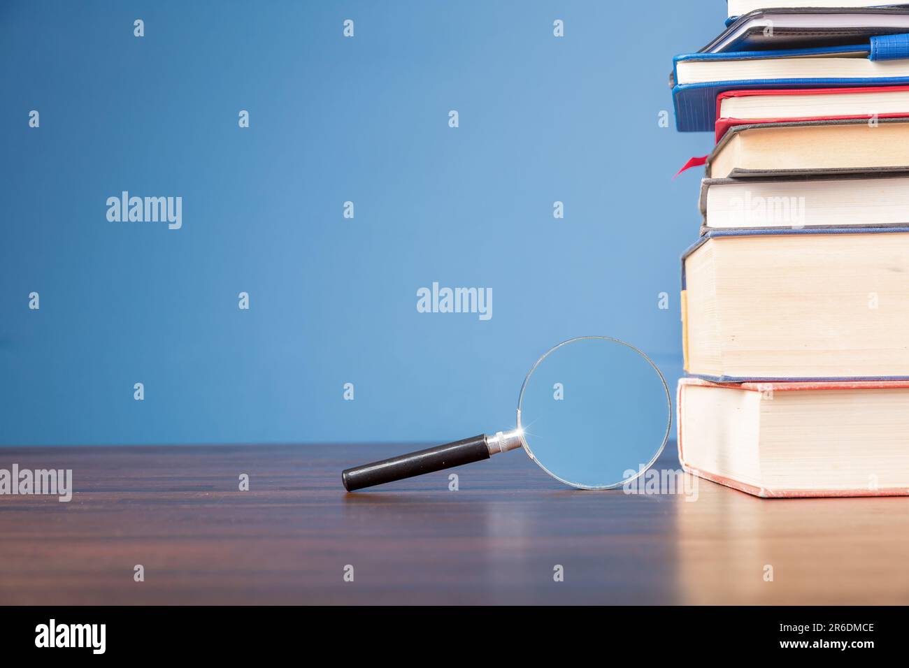 Pila libro con lente d'ingrandimento su scrivania di legno in biblioteca di informazioni della scuola o dell'università, concetto per l'istruzione, la lettura, lo studio, copia spazio su b Foto Stock