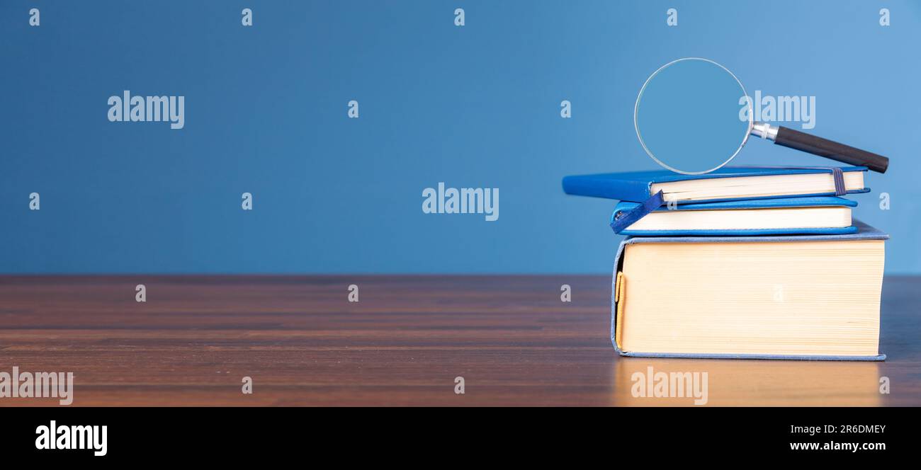 Pila libro con lente d'ingrandimento su scrivania di legno in biblioteca di informazioni della scuola o dell'università, concetto per l'istruzione, la lettura, lo studio, copia spazio su b Foto Stock
