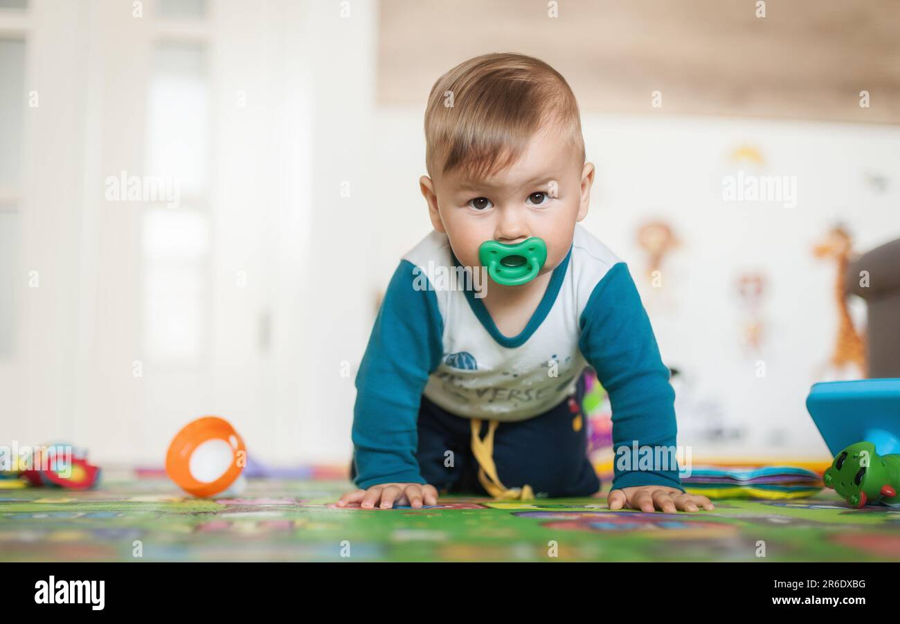 Cute baby boy striscia sul pavimento di casa, esplorare il mondo e imparare a muoversi. Vista frontale. Amore ed emozione familiare Foto Stock