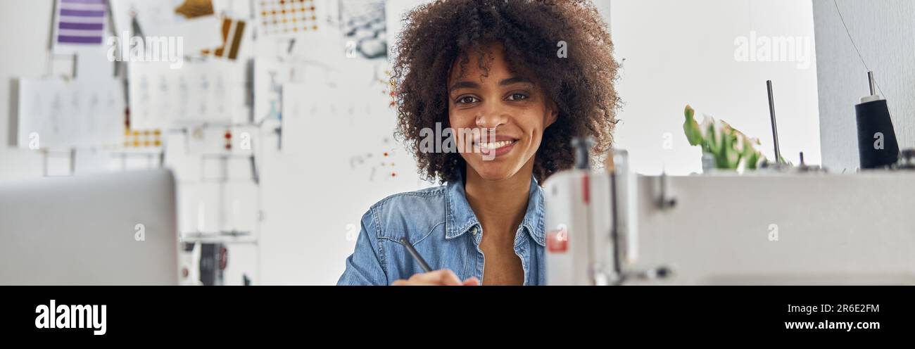 Donna afroamericana sorridente con il laptop si siede sul posto di lavoro in s Foto Stock