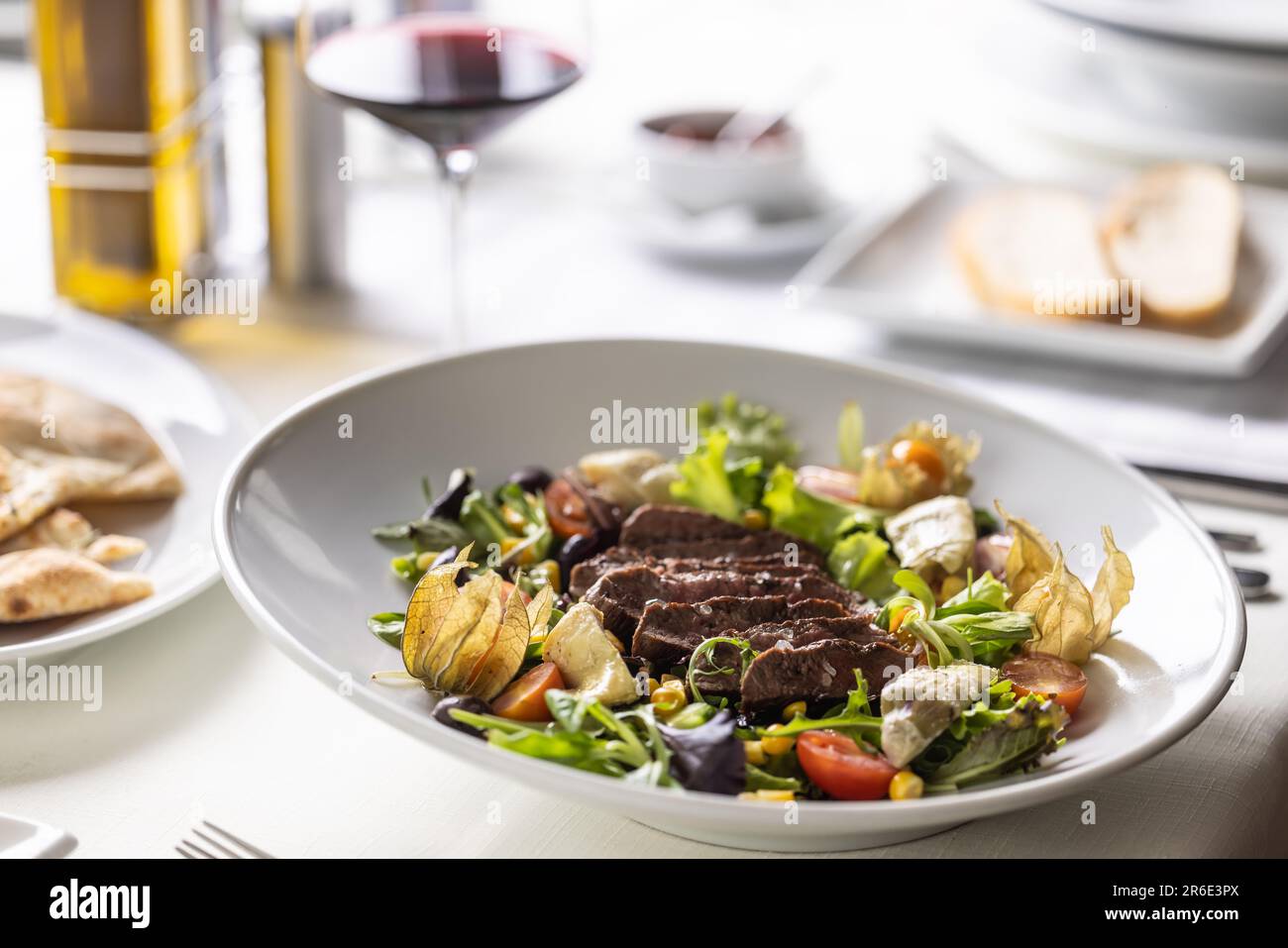 Bistecca di manzo affettata su un'insalata mista con verdure, physalis, pomodori ciliegini serviti con vino. Foto Stock