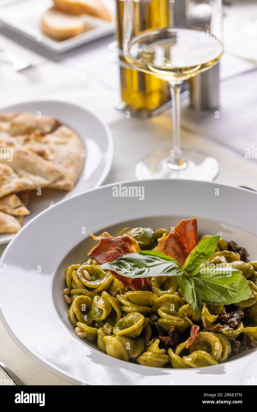Orecchiette con pesto genovese verde e speck tirolese condite con foglie di basilico. Foto Stock