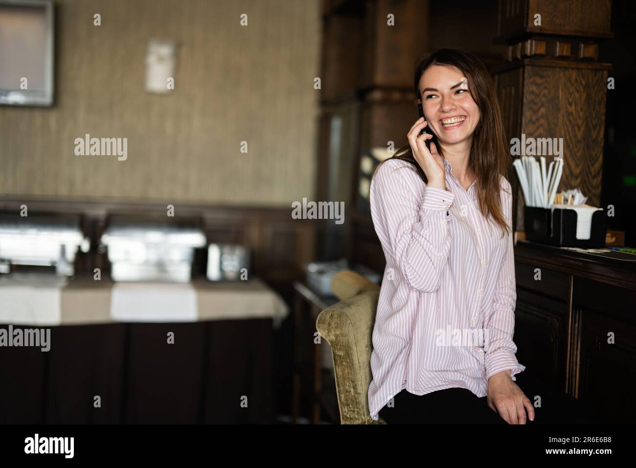 Giovane bella bruna donna seduta vicino al bancone del bar, parlando al telefono e ridendo. Foto Stock
