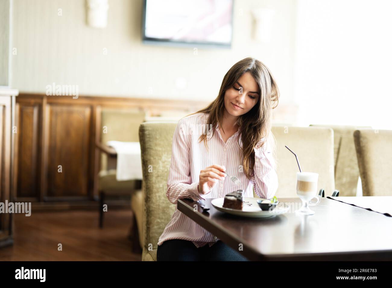 Giovane donna bella brunette sedersi nel bar ristorante caffetteria al coperto e mangiare torta di cioccolato Brownie dessert. Foto Stock