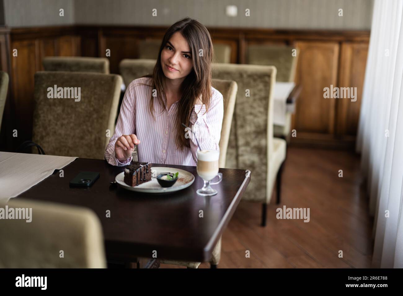 Giovane donna bella brunette sedersi nel bar ristorante caffetteria al coperto e mangiare torta di cioccolato Brownie dessert. Foto Stock