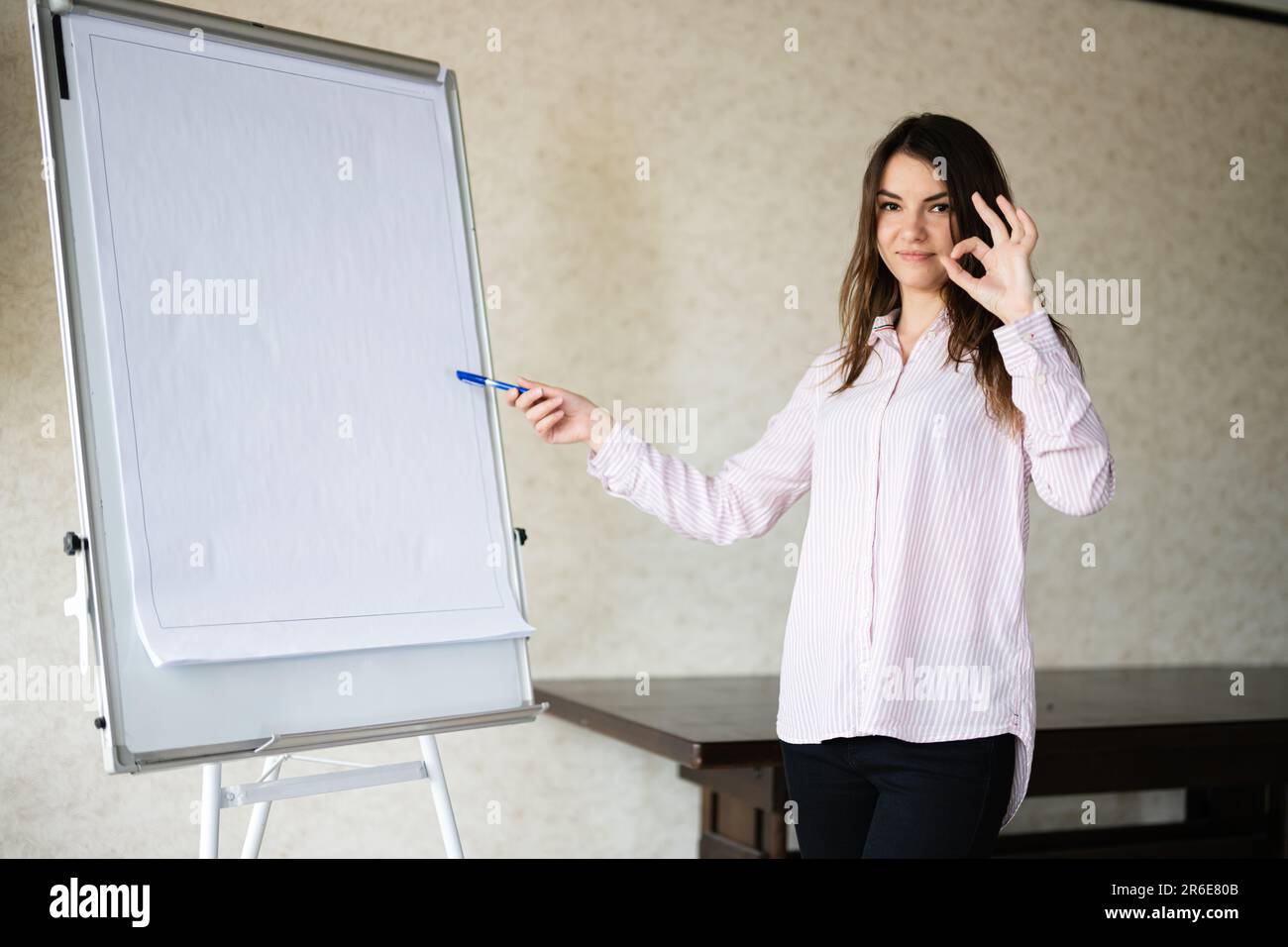 Giovane donna parlante caucasica coach show su lavagna bianca, OK segno. Il team leader femminile approva le idee di progetto. Foto Stock